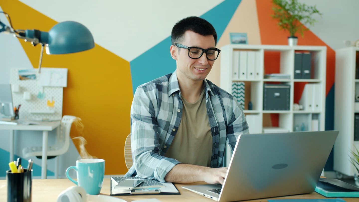 Hombre con gafas trabajando en un portátil en un escritorio.
